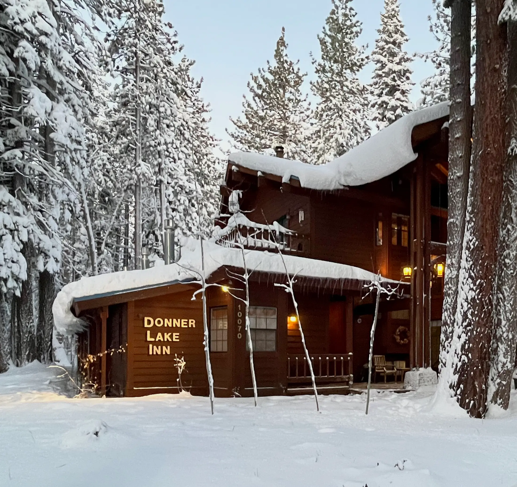Donner Lake Inn in deep fresh snow at dusk, the Donner Lake Inn sign and windows lit warm under snow-laden pines