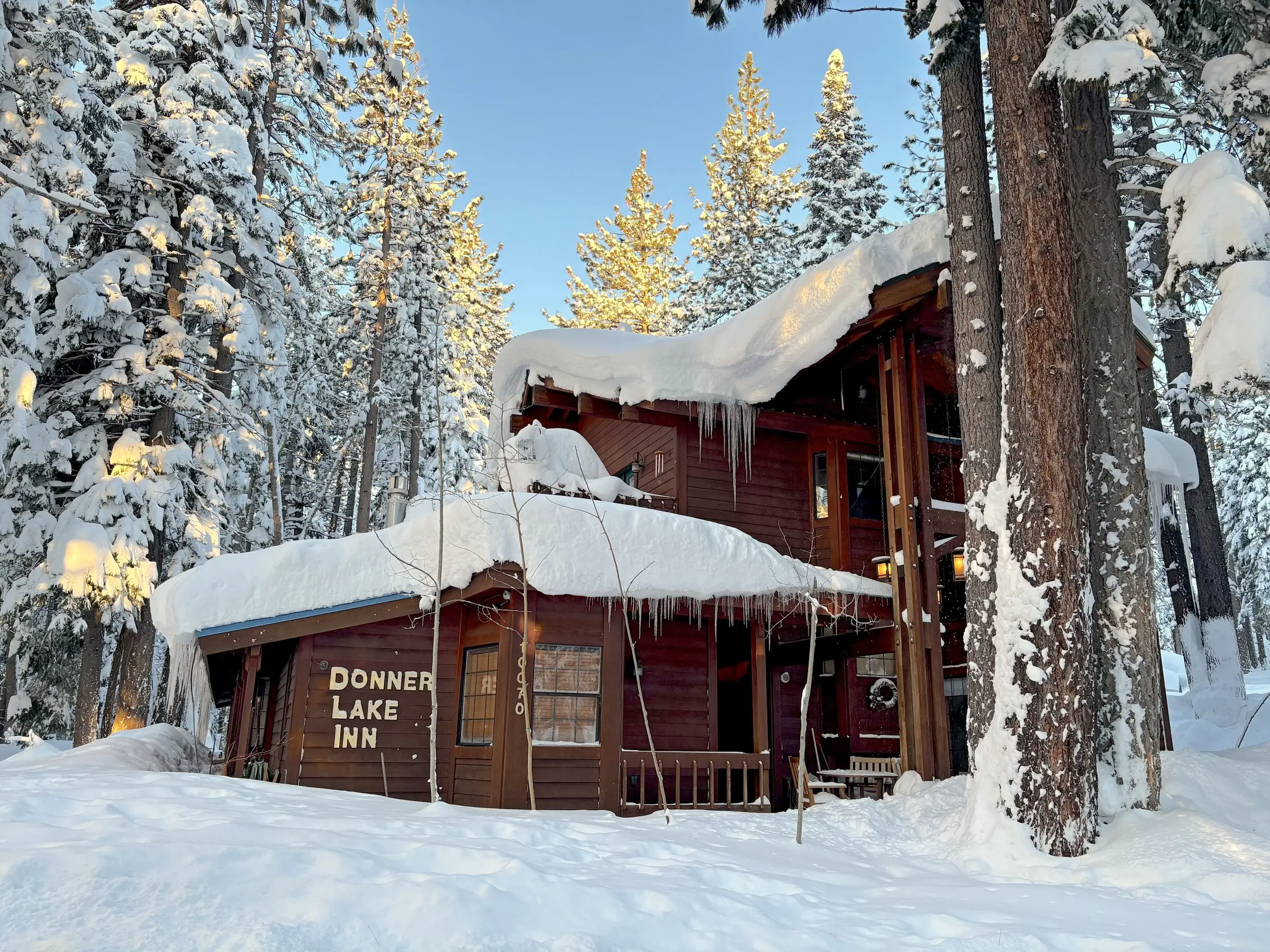 Donner Lake Inn under deep fresh snow on a clear morning, sun on the treetops and icicles along the roofline